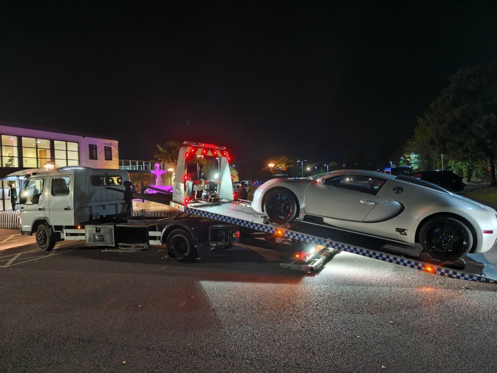 White Bugatti Veyron loaded onto a flatbed recovery truck at night