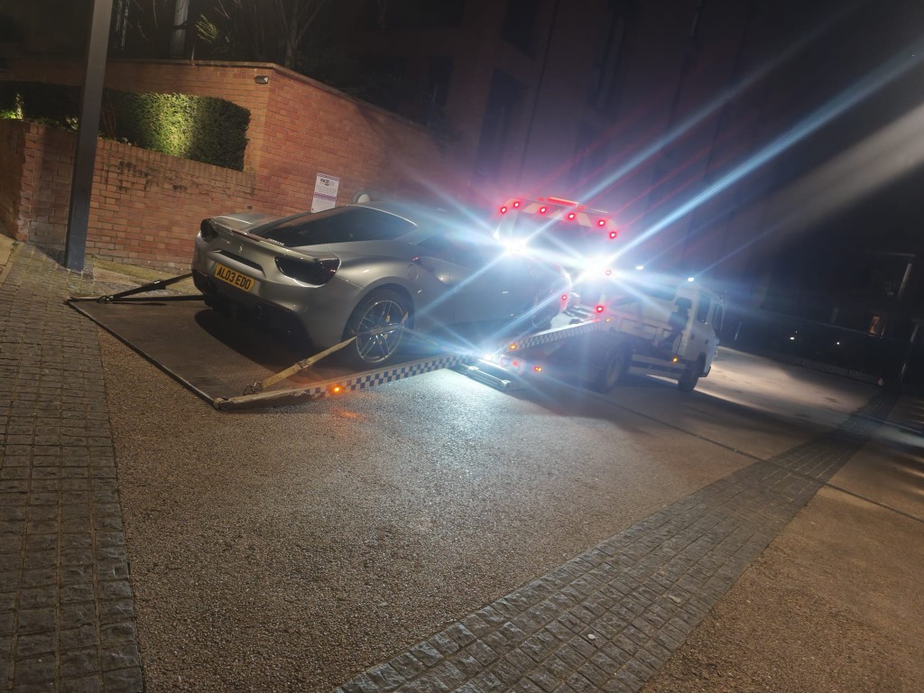 Silver Ferrari on tilt-bed recovery truck at night