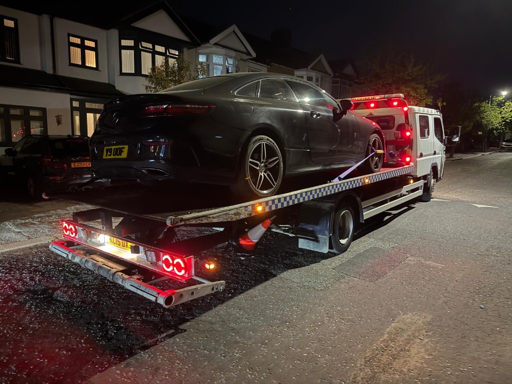 Black Mercedes coupe on flatbed recovery truck at night