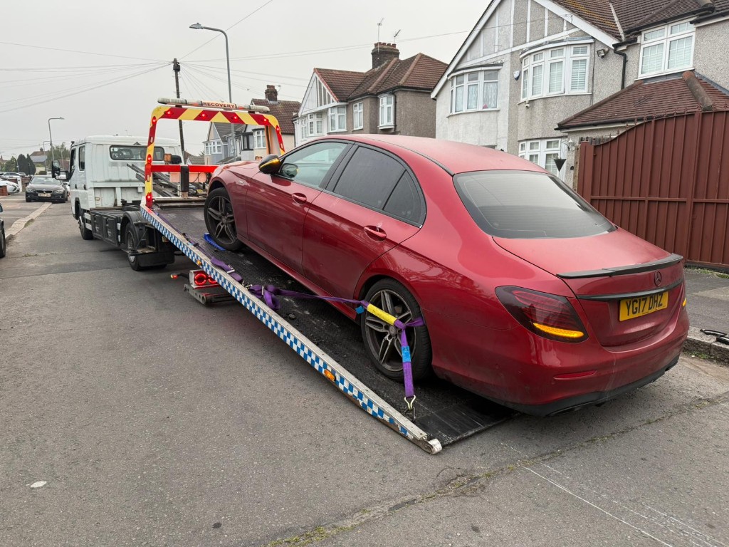 Red Mercedes-Benz sedan secured on tilt-bed recovery truck